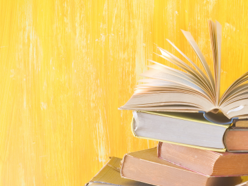 A stack of books with the top one fanned open in front of a yellow backdrop